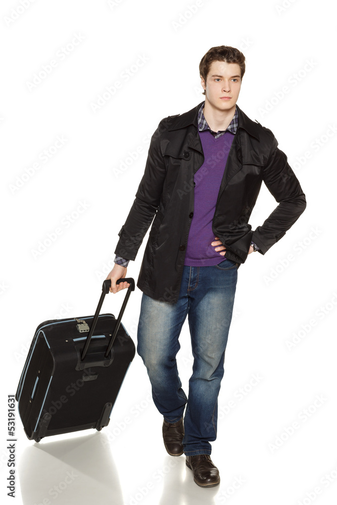 Young man in jeans and jacket walking with travel suitcase Young man in jeans and jacket walking with travel suitcase