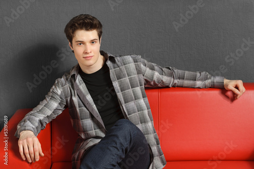 Man sitting on red sofa with hand rested on the sofa