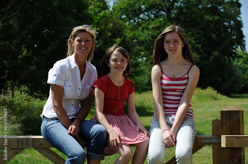 Portrait of a woman and two girls sitting on a fence Portrait of a woman and two girls sitting on a fence