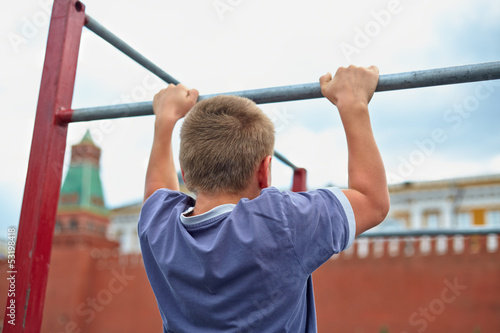 Boy does chin-ups against kremlin wall, back view