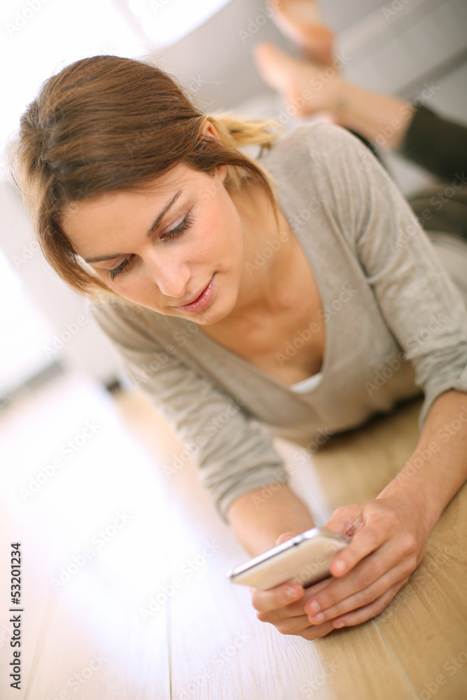 Naklejka premium Young woman laying on the floor with smartphone