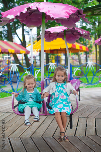 Two little fashion lovely sisters ride on the carousel in the