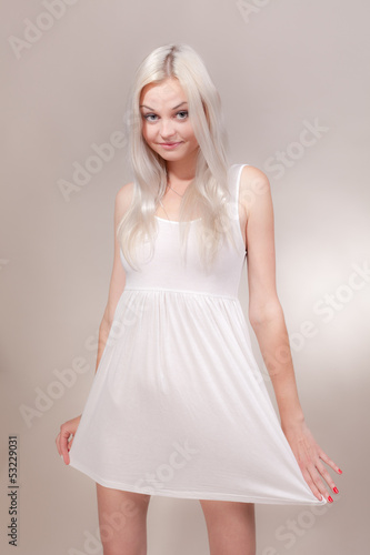 Beautiful girl in a short white dress on a gray background.