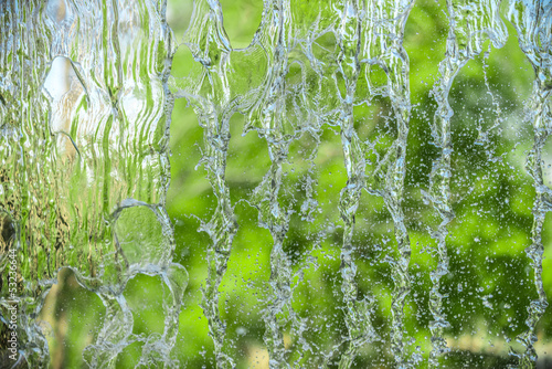 Behind a waterfal. A beautiful view of a blue sky and green trees through the falling water cascade.