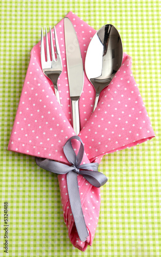 Fork spoon and knife in napkin on fabric checkered background