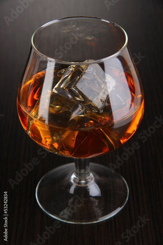 Brandy glass with ice on wooden background