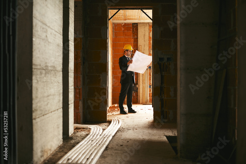Architect standing in house under construction with building pla