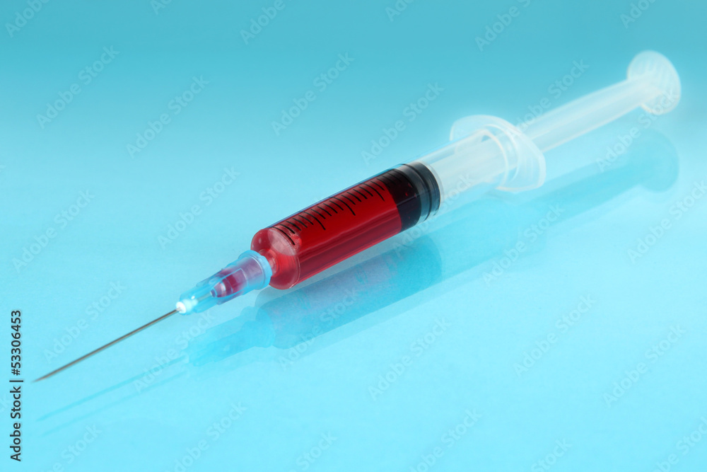 Plastic disposable syringe filled with blood on blue background Plastic disposable syringe filled with blood on blue background