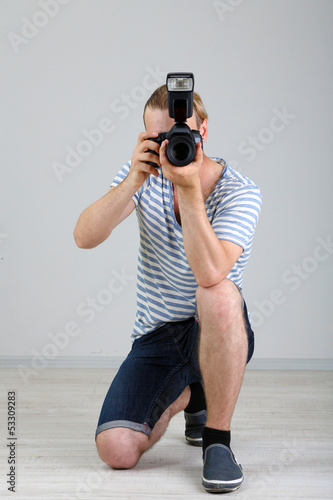 Handsome photographer with camera, on gray background © Africa Studio