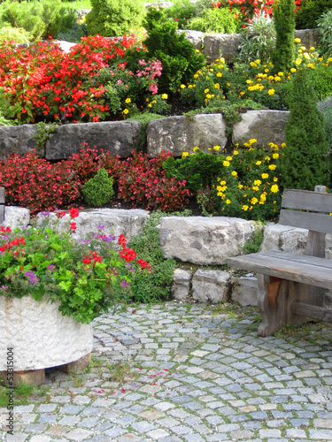 Stone wall, bench and plants on colorful landscaped garden.
