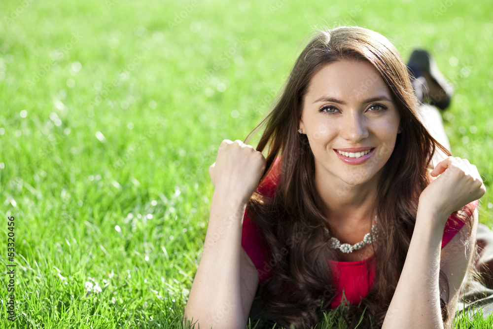 Naklejka premium Portrait of young woman lying on a green lawn