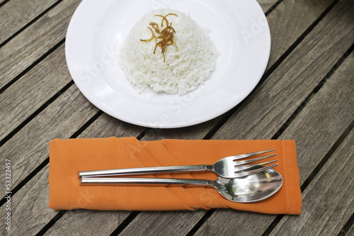 Fork and spoon on orange tablemat with rice on white plate