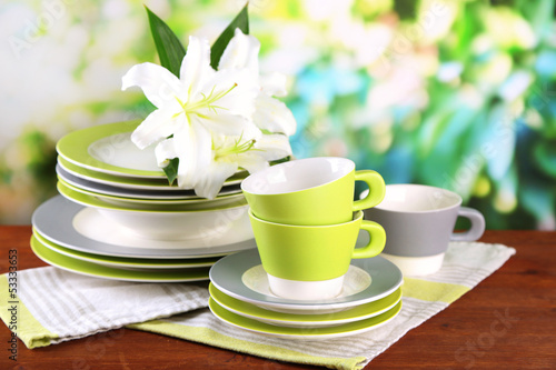 Fototapeta Naklejka Na Ścianę i Meble -  Empty plates and cups on wooden table on green background