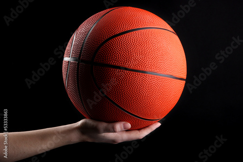 Basketball in woman hand on black background © Africa Studio