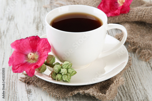 Cup of coffee and pink mallow flowers on wooden background