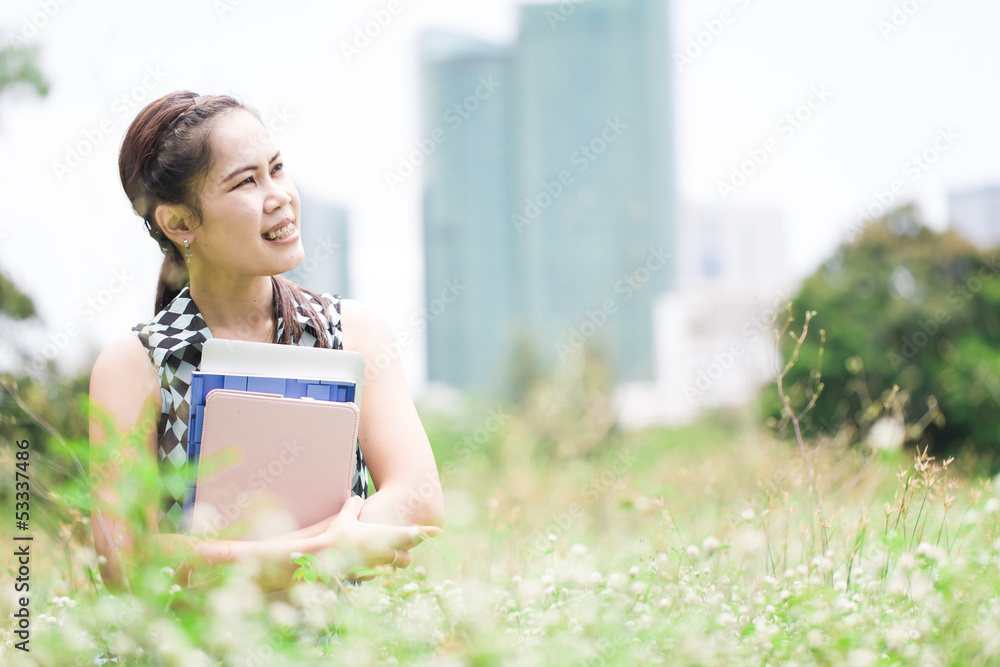 Fototapeta premium Young woman sitting on green grass and hug book