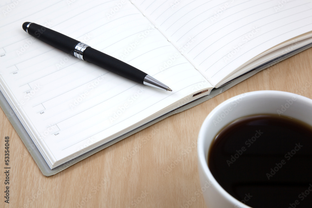 Cup of coffee on a wooden table with book and pen Cup of coffee on a wooden table with book and pen