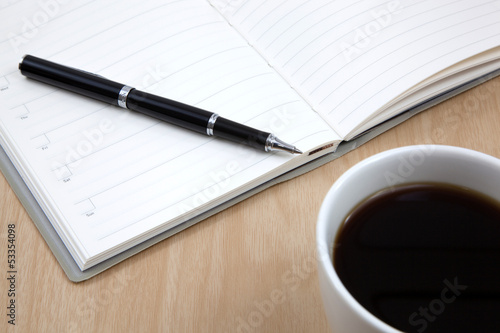 Cup of coffee on a wooden table with book and pen