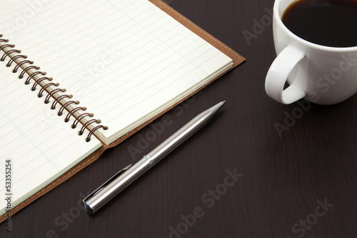 Cup of coffee on a wooden table with book and pen
