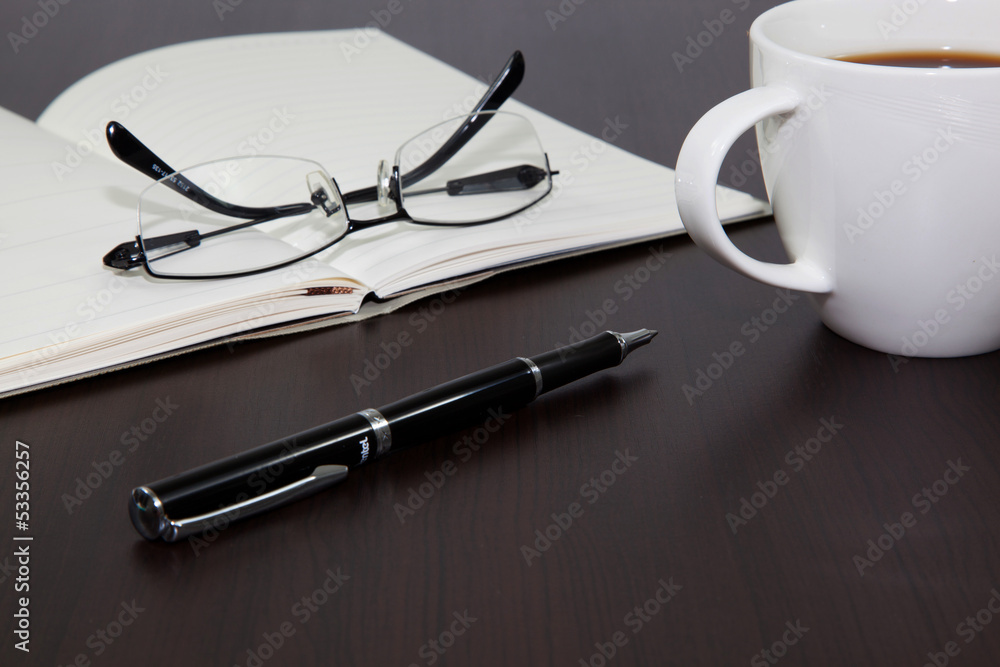 Cup of coffee on a wooden table with book and pen Cup of coffee on a wooden table with book and pen