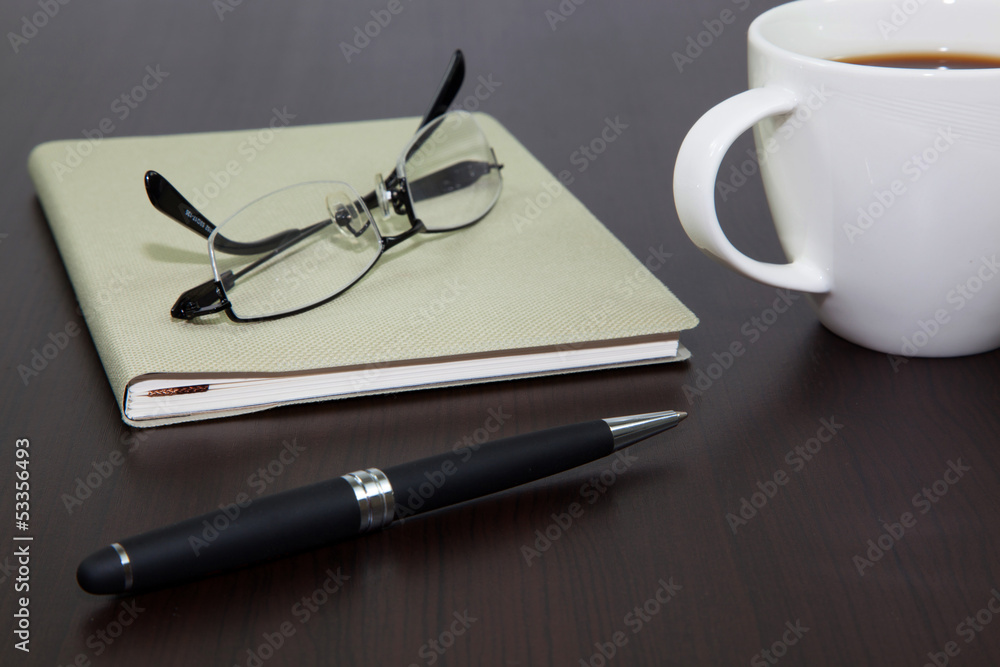 Fototapeta premium Cup of coffee on a wooden table with book and pen