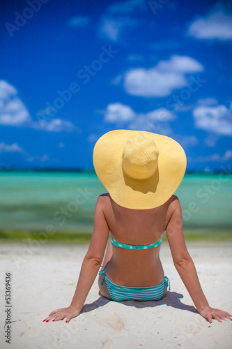 Woman sitting on beach holding beach hat enjoying summer