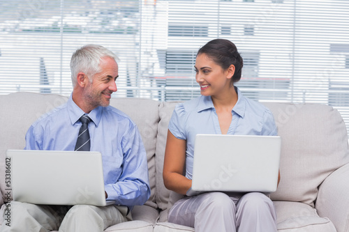 Business people using their laptops and smiling at each other