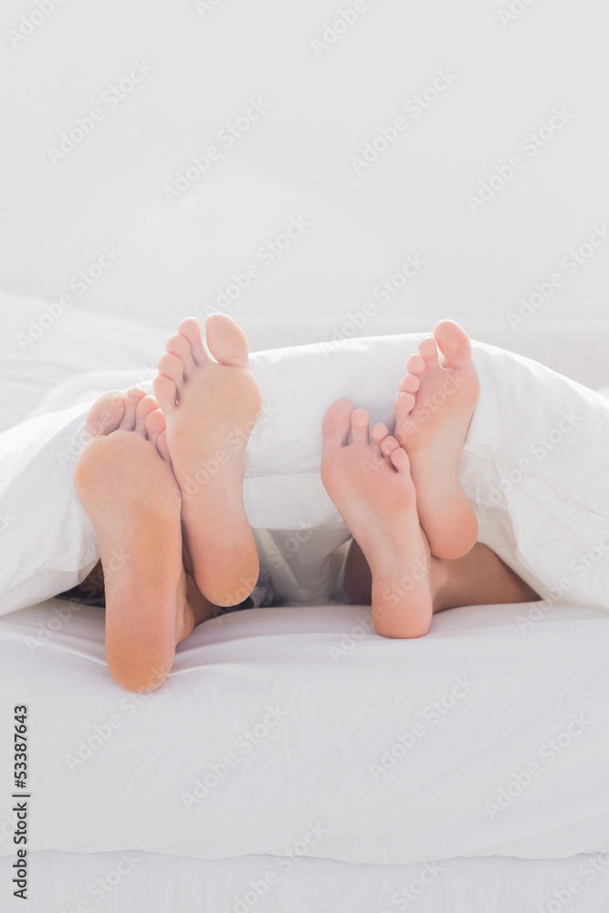 Couple crossing their feet under the duvet Couple crossing their feet under the duvet