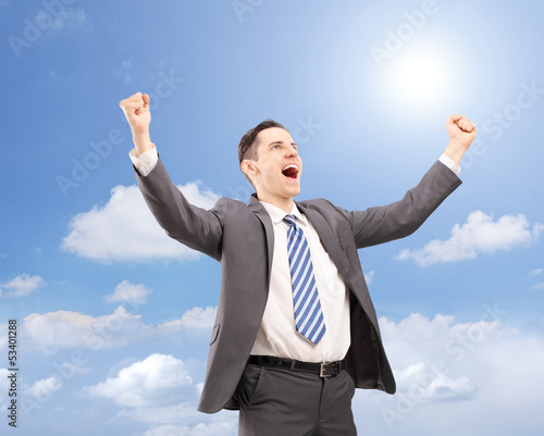 Young satisfied businessman gesturing happiness against blue sky