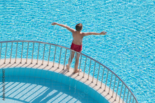 Boy sunbathing on edge of pool raised his hands up