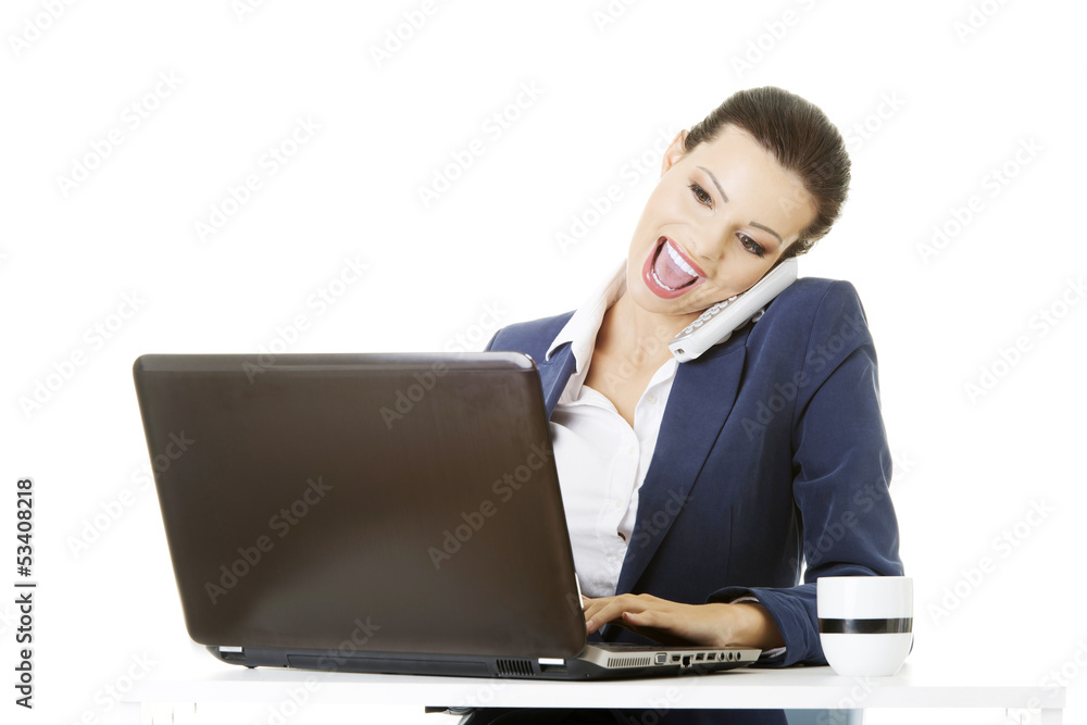 Smiling young business woman speaking on phone while using lapto Smiling young business woman speaking on phone while using lapto