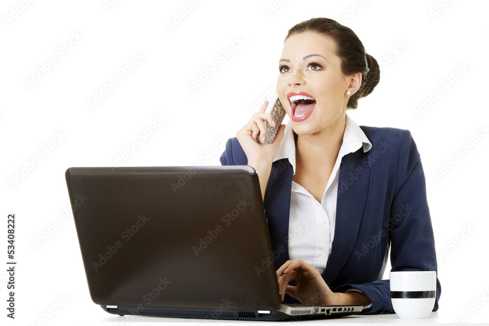 Smiling young business woman speaking on phone while using lapto Smiling young business woman speaking on phone while using lapto