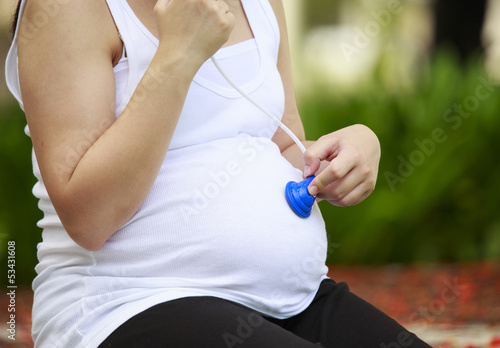 pregnant woman listening her baby with a stethoscope at park