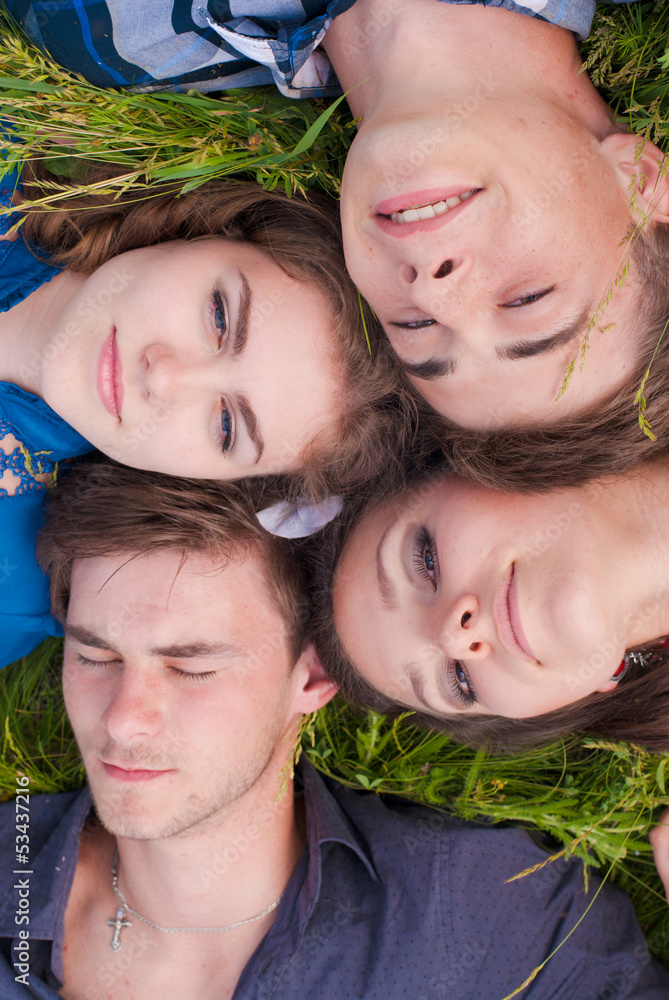 Four happy teenage friends lying together on green grass Four happy teenage friends lying together on green grass