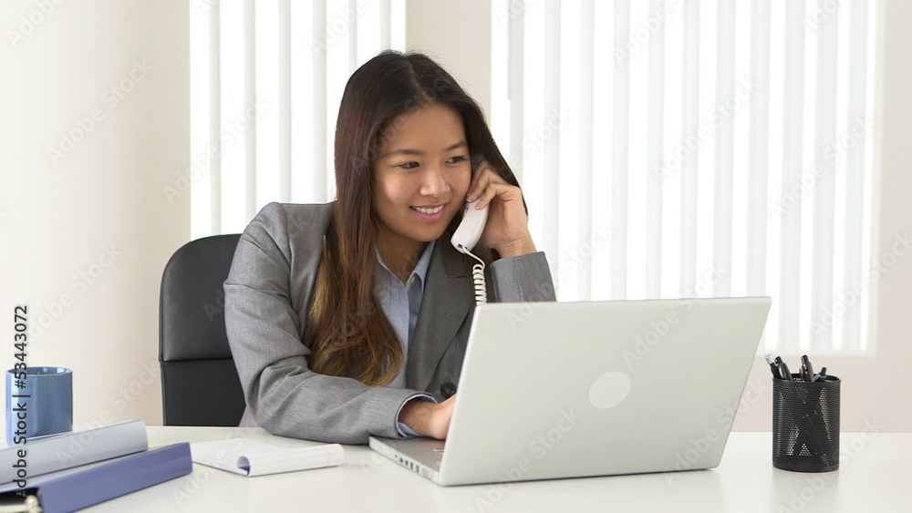 Asian businesswoman talking on phone while working at desk Asian businesswoman talking on phone while working at desk