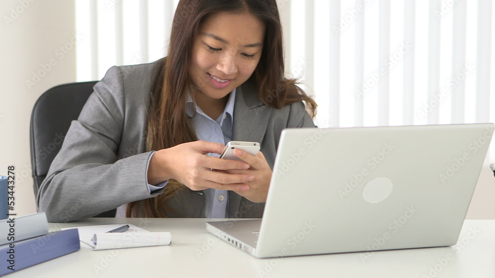 Asian businesswoman texting while working at desk Asian businesswoman texting while working at desk