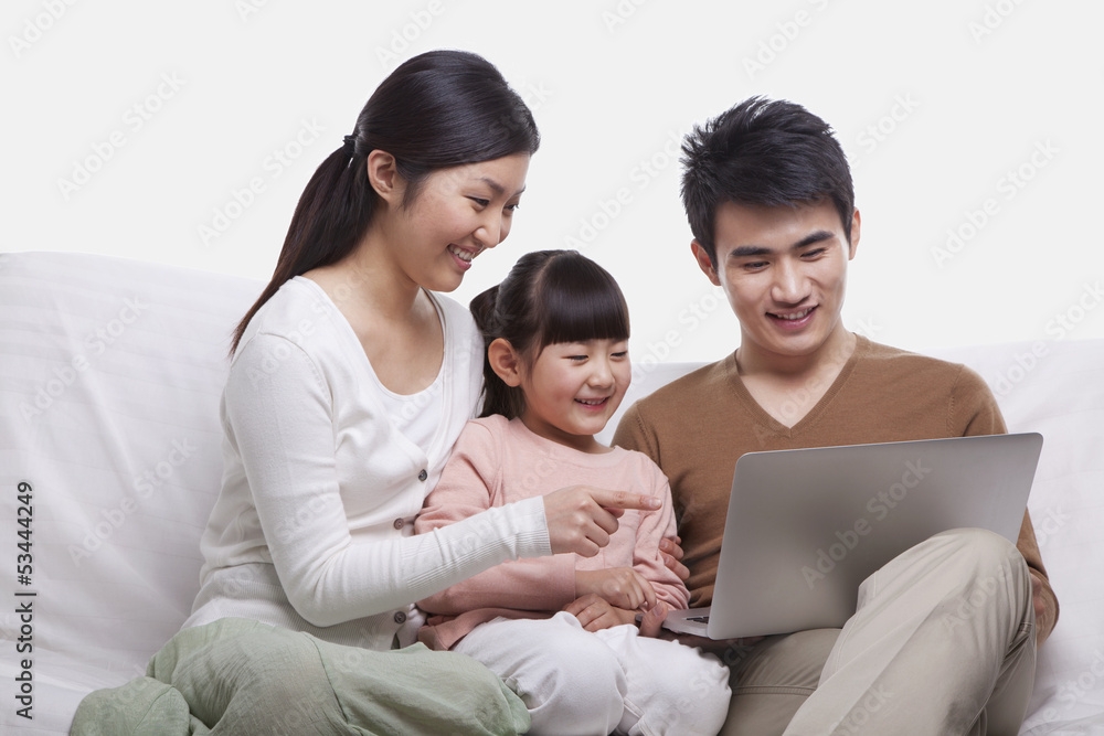 Family sitting on the sofa looking at laptop, studio shot Family sitting on the sofa looking at laptop, studio shot