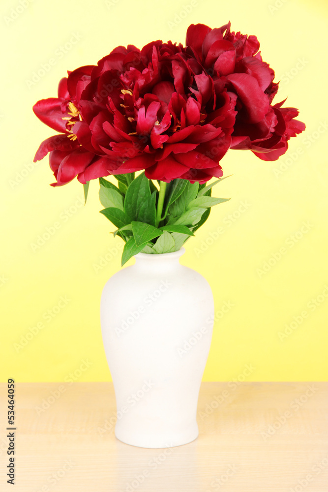 Fototapeta premium Beautiful peonies in vase on table on yellow background