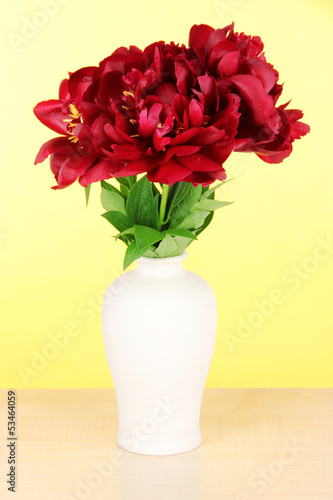 Beautiful peonies in vase on table on yellow background