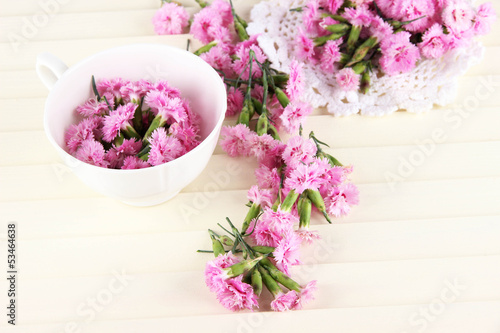 Many small pink cloves in cup and on napkin on wooden