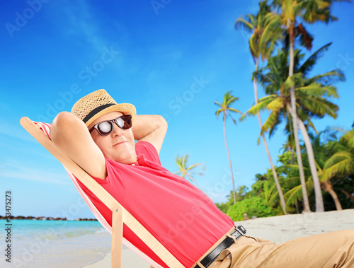 Mature male tourist enjoying on a beach next to a sea and palm t