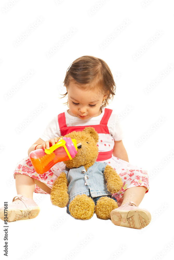 Toddler girl givng juice to her bear toy