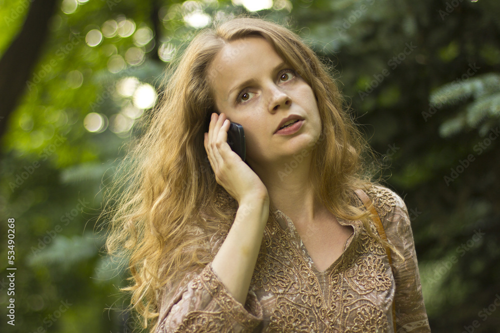 Naklejka premium beautiful girl talking on the phone in the green forest