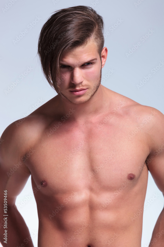 topless young man stands with hands at back