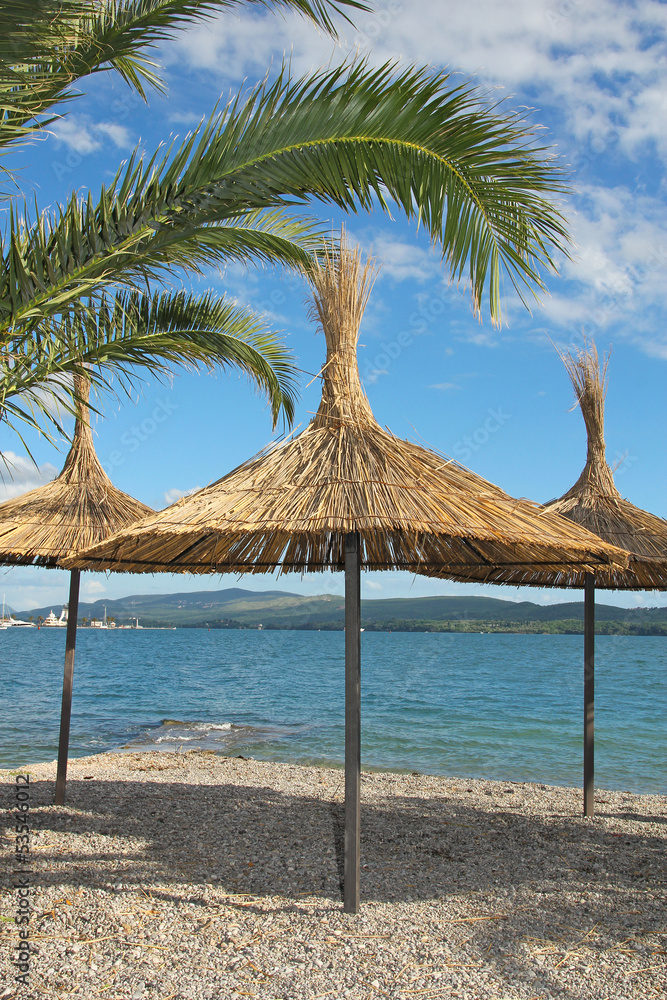 straw umbrellas and palm leafs on the beach