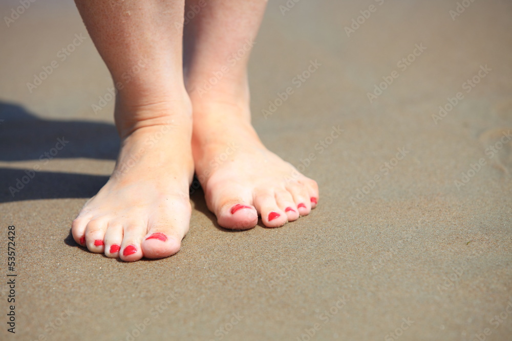 Woman feet with red pedicure relaxing on sand