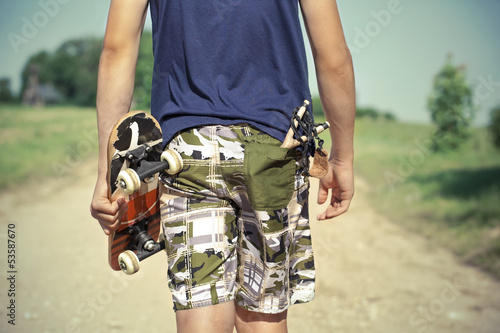 Boy with skateboard and slingshot in pocket on rural road
