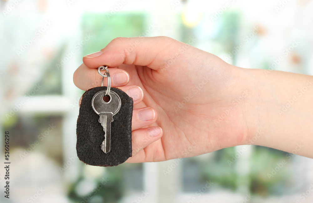 Key with leather trinket in hand on window background Key with leather trinket in hand on window background