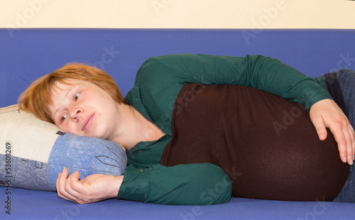Pregnant woman lying on a sofa thinking