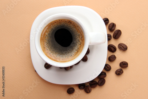 Cup of coffee with coffee beans on beige background